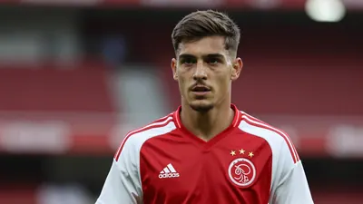 A determined 25-year-old Ajax midfielder, athletic build, in a plain dark red and white training top, against a blurred...