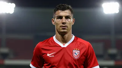 A 25-year-old male football player, waist-up, with a determined expression, wearing a red and white kit