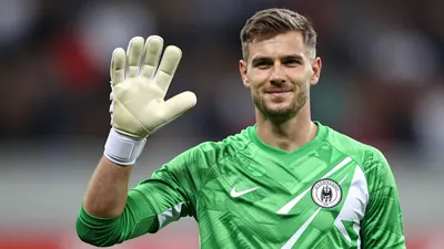 A 34-year-old German goalkeeper with a strong build, wearing a green and white jersey, with a white goalkeeper's glove on...