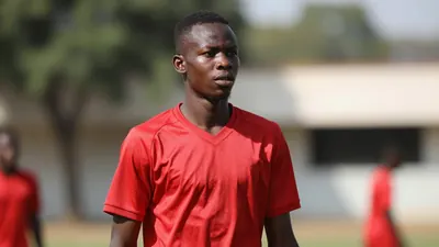 A 17-year-old Guinean midfielder with a lean build and short black hair, wearing a solid red jersey made of smooth...