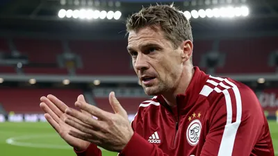A close-up shot of a 28-year-old, 5'11" AFC Ajax assistant coach, wearing a dark red and white polyester training top...