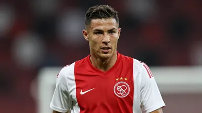 A tight action crop of an anonymous Ajax player in a red jersey with white sleeves, looking focused with a determined...