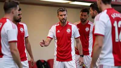 A 35-year-old, 5'10" AFC Ajax coach with a rugged build, stands intensely on the Johan Cruijff Arena's tunnel wall, his...