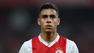 A close-up shot of a young, anonymous Ajax player with a determined look on his face, wearing a red and white jersey with...