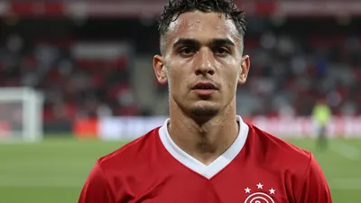 Mid-30s Ajax midfielder, athletic build, intense gaze, head-and-shoulders shot, dark red home jersey with clean white...
