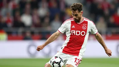 A focused AFC Ajax player in a red and white striped jersey, mid-kick during a Conference League match