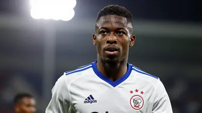 25-year-old Nigerian striker, lean and athletic, wearing Ajax's all-white kit with blue trim, head-and-shoulders shot...