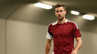 A medium shot of a 30-year-old, 5'10" right midfielder with a rugged build, dressed in a plain, dark red and white...