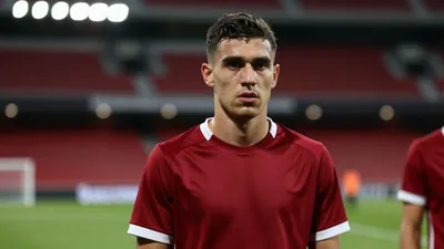 A 20-year-old defender with a rugged build and short, dark hair, clad in a dark red and white plain cotton training top...