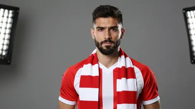 A 26-year-old, dark-haired, bearded, and muscular player in a red and white striped jersey, with a white collar and a red...