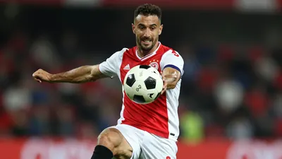 A photorealistic image of an anonymous Ajax player, aged 25-30, with a strong build, wearing a red jersey with white...