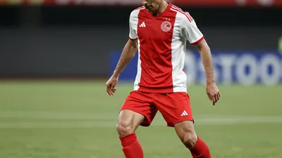 A photorealistic image of an anonymous Ajax player in a red and white jersey, with a white shirt and red shorts, playing...