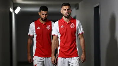 A photorealistic image of an anonymous Ajax player, aged 25-30, wearing a red jersey with white sleeves and white shorts...