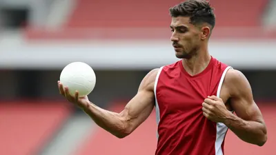 Mid-30s anonymous Ajax staff member, athletic build, waist-up, holding a glossy white lottery ball in one hand, other...
