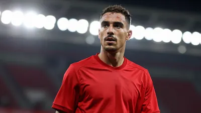 A mid-30s anonymous Ajax player in a solid red jersey, waist-up, focused expression, background blurred stadium lights...