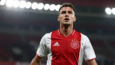 Mid-30s Ajax forward, athletic build, intense expression, head-and-shoulders, dark red home shirt with white sleeves...