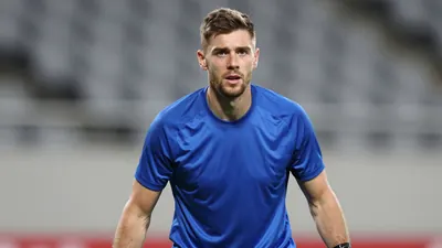 Photorealistic portrait of a 34-year-old male goalkeeper in a tight action crop, wearing a solid blue jersey with smooth...