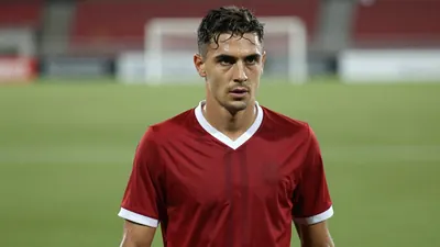 Mid-30s athletic midfielder, lean build, intense gaze, waist-up in dark red jersey with white trim, plain cotton fabric...