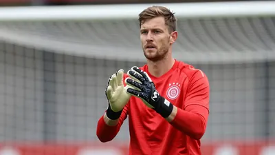A 30-year-old German goalkeeper with a clean red jersey and black gloves, standing in a focused stance with his hands ready