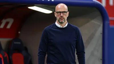 A 35-year-old, balding, bespectacled coach in a dark blue, long-sleeved shirt with a white collar, stands in the tunnel...