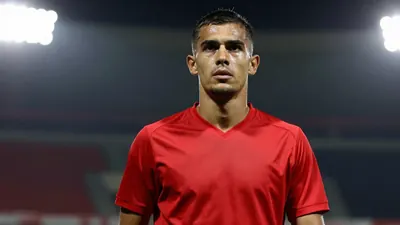 A 25-year-old male football player, wearing a solid red jersey made of smooth fabric, photographed with an 85mm f/1.4...