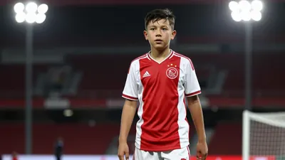11-year-old midfielder, Ajax academy, wearing solid red jersey and white shorts, intense focus on determined young face