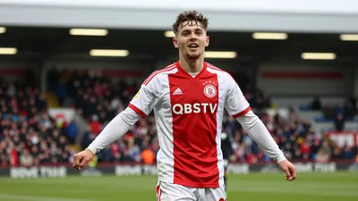 A young Ajax player in a red and white kit, celebrating a goal in the Conference League match against Shelbourne FC...