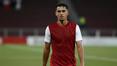 Mid-30s athletic forward, lean build, dark curls framing a focused face, wearing an unmarked dark-red jersey with white...