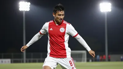 A 30-year-old Ajax defender in a red jersey with white sleeves, playing a one-on-one against an opponent