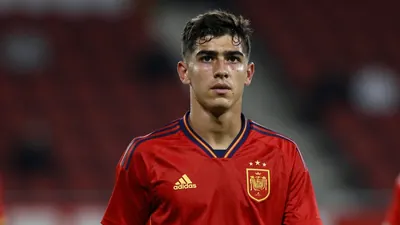 Photograph of a young Spanish football player, 19 years old, with a strong build, wearing a solid red jersey, taken with...