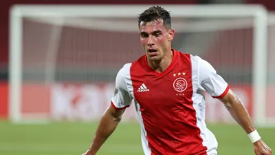 A mid-30s Ajax midfielder in a plain dark-red shirt with white sleeves, waist-up, captured mid-roll on the grass, face...