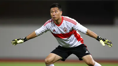 A tight action crop of a 30-40-year-old male goalkeeper in a white jersey with a red stripe, black shorts, and white...