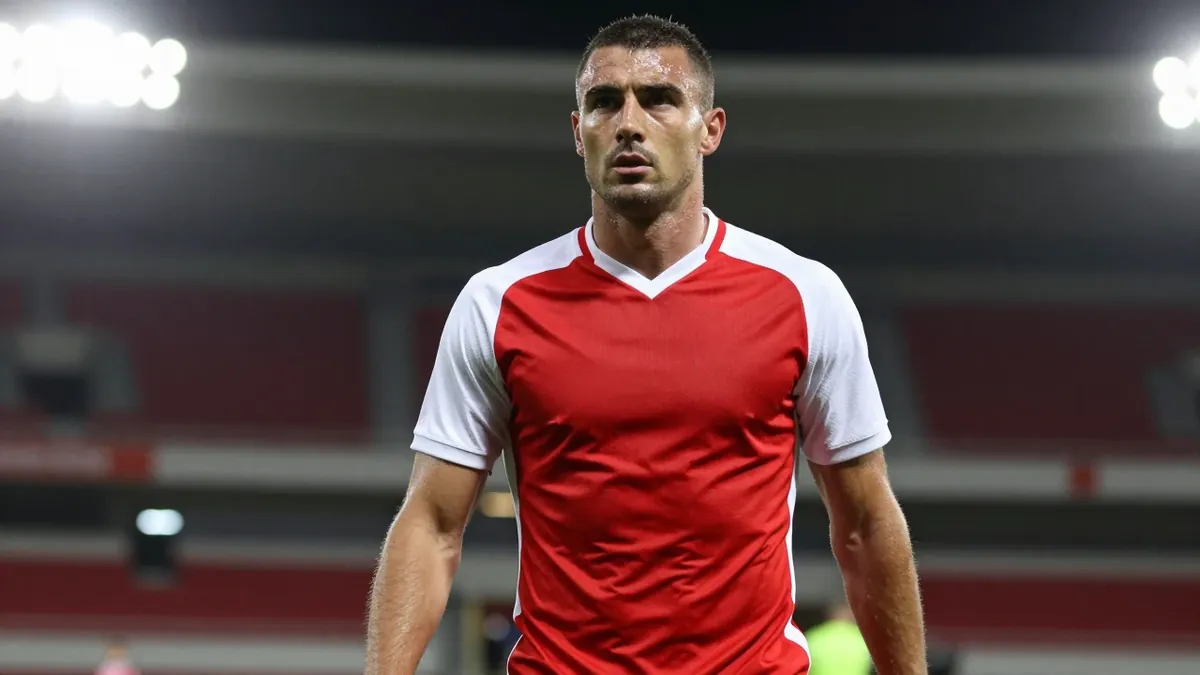 A 30-year-old football player with a strong build, wearing a red and white kit, photographed with an 85mm f/1.4 lens...