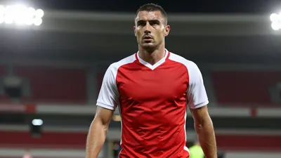 A 30-year-old football player with a strong build, wearing a red and white kit, photographed with an 85mm f/1.4 lens...