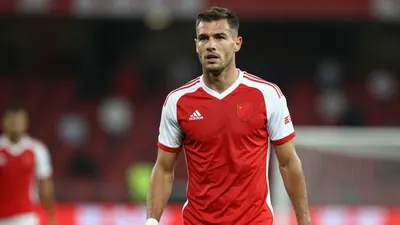A 22-year-old football player with a muscular build and short hair, wearing a red and white kit, photographed with a 85mm...