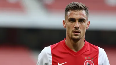 A mid-30s anonymous Ajax forward, athletic build, intense gaze, head-and-shoulders shot, wearing an unmarked dark red...