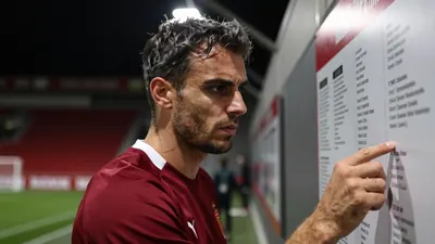 A close-up shot of a 25-year-old, 5'11" male coach, with a rugged, weathered complexion, wearing a plain, dark red and...