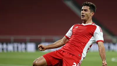 A young, energetic, and athletic football player, around 20-25 years old, with a muscular build, wearing a solid red and...