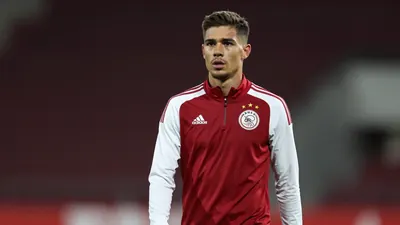 A determined, 25-year-old Ajax midfielder, wearing a plain dark red and white training top, stands waist-up, eyes fixed...